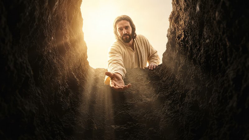 A person in a light-colored robe leans down into a deep, rocky hole, extending a hand toward someone below. Sunlight shines from above, illuminating the figure.